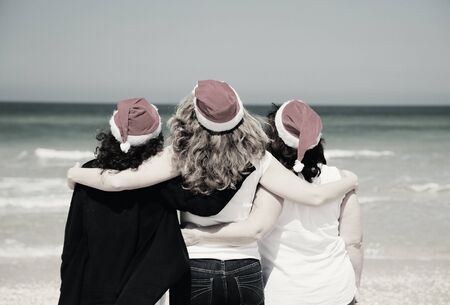 Three beautiful women wearing christmas hat walking on the seasideの写真素材
