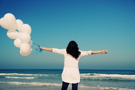 woman holding white balloons on seasideの写真素材