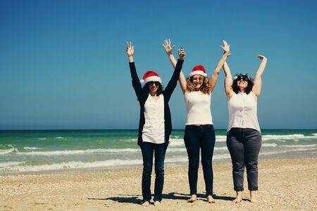 Three beautiful women wearing christmas hat walking on the seasideの写真素材