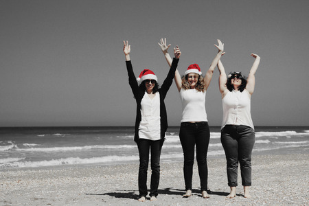 Three beautiful women wearing christmas hat walking on the seasideの写真素材