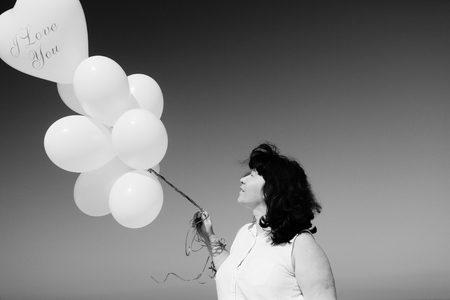 woman holding white balloons on seasideの写真素材