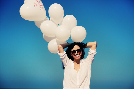 woman holding white balloons on seasideの写真素材