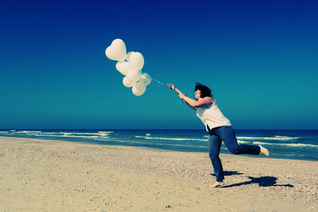 woman holding white balloons on seasideの写真素材