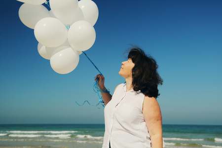 woman holding white balloons on seasideの写真素材