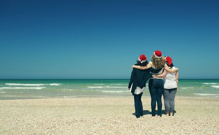 Three beautiful women wearing christmas hat walking on the seasideの写真素材