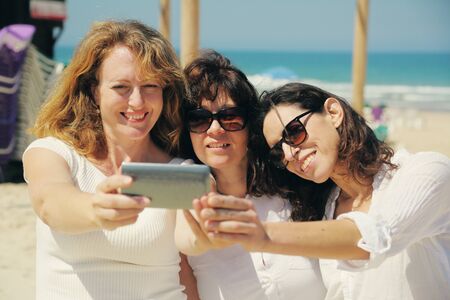 three best friends walking on the seaside making selfie photoの写真素材