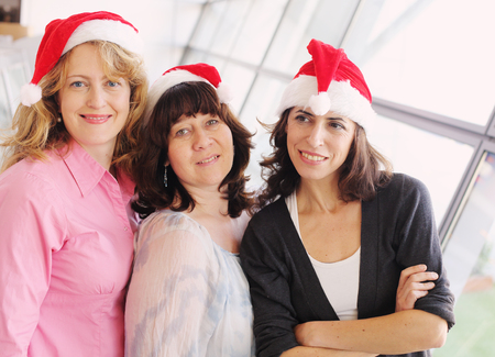Portrait of three beautiful real women wearing christmas hatの写真素材