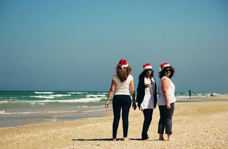 Three beautiful women wearing christmas hat walking on the seasideの写真素材