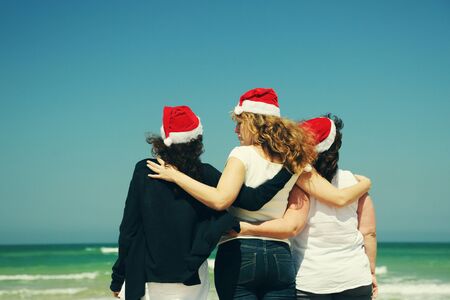 Three beautiful women wearing christmas hat walking on the seasideの写真素材