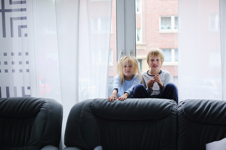 Portrait of brother and sister in the morning sitting near the window at homeの写真素材
