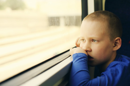 Sad 8 years old boy looking through the window in the trainの写真素材
