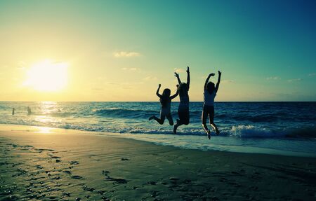 Three girlfriends jumping on the beach at sunsetの写真素材
