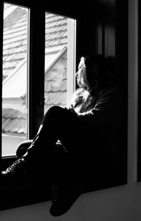 Portrait of beautiful sad woman looking throught the windowの写真素材