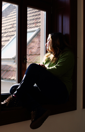 Portrait of beautiful sad woman looking throught the windowの写真素材