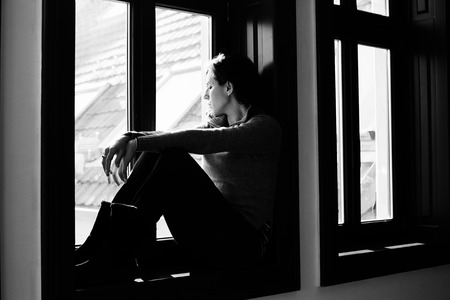 Portrait of beautiful sad woman looking throught the windowの写真素材