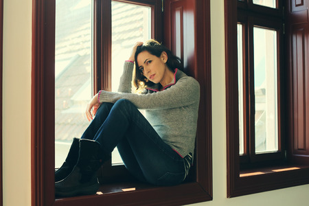 Portrait of beautiful sad woman looking throught the windowの写真素材