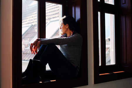 Portrait of beautiful sad woman looking throught the windowの写真素材