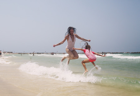 Portrait of happy  real beautiful young girls jumping on seasideの写真素材