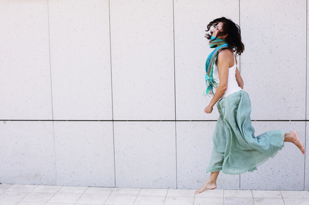 Portrait of smiling beautiful woman in turquoise skirt walking against of city grey wallの写真素材