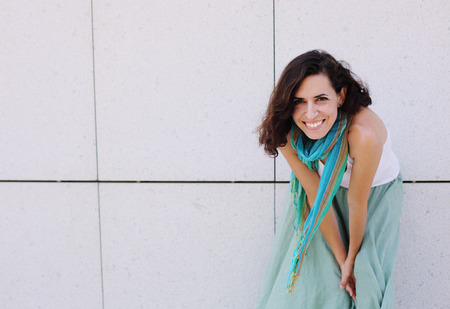 Portrait of smiling beautiful woman in turquoise skirt standing against of city grey wallの写真素材