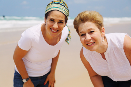 Portrait of two beautiful 45 years old women walking on seasideの写真素材