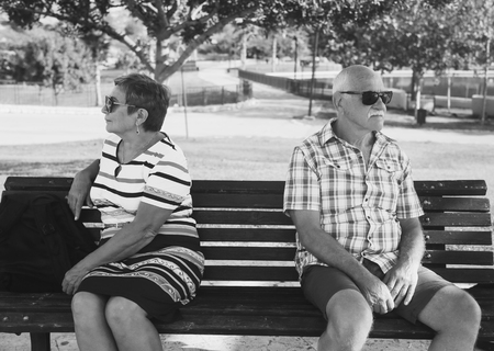 Elderly couple are sitting upset on a bench in a park . Family quarrel.の写真素材