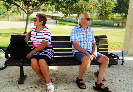 Elderly couple are sitting upset on a bench in a park . Family quarrel.の写真素材