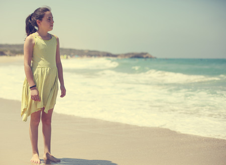 12 years old girl teen girl in yellow dress walking on seaside. Summer vacationの写真素材