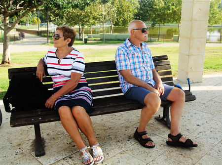 Elderly couple are sitting upset on a bench in a park . Family quarrel.の写真素材