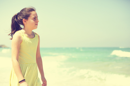 12 years old girl teen girl in yellow dress walking on seaside. Summer vacationの写真素材