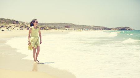 12 years old girl teen girl in yellow dress walking on seaside. Summer vacationの写真素材