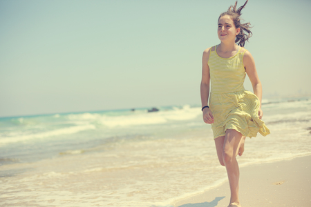 12 years old girl teen girl in yellow dress walking on seaside. Summer vacationの写真素材