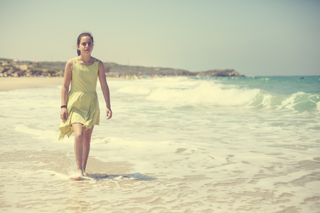12 years old girl teen girl in yellow dress walking on seaside. Summer vacationの写真素材