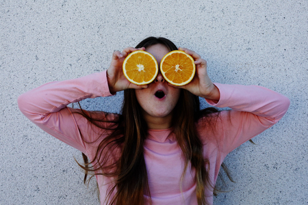 Portrait of beautiful teenage girl with orange fresh fruit outdoorの写真素材