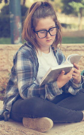 Portrait of tenage girl sitting outdoor reading a bookの写真素材