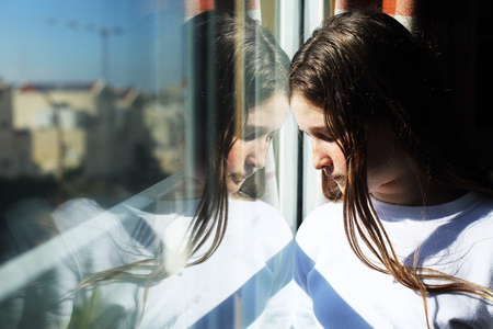 attractive sad teenage girl looking out of the windowの写真素材