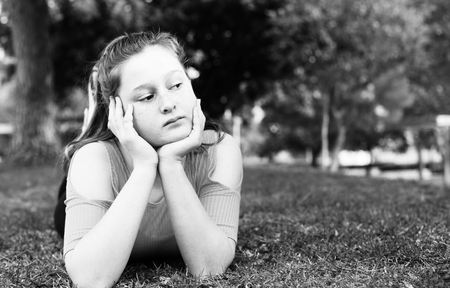 Beautiful teenage girl lying on green meadow in city parkの写真素材