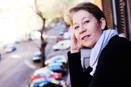 beautiful mature woman standing on the balcony looking to the streetの写真素材