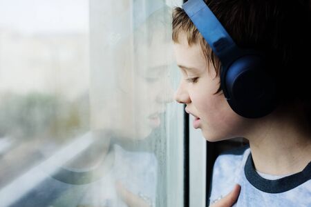 Teenage 12 years old boy looking through the window on the rainの写真素材