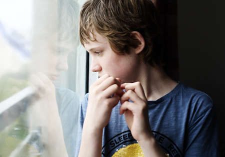 Cute 12 years old autistic boy looking through the windowの写真素材