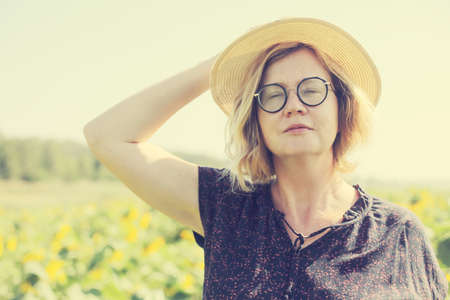 Portrait of happy mature woman with hat enjoying of freedom in the sunflowers fieldの写真素材