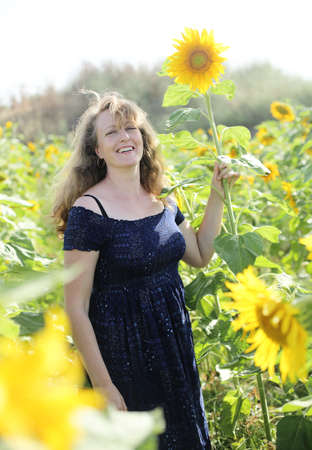 Beauty mature woman with sunflower enjoying freedom on summer sunflower fieldの写真素材