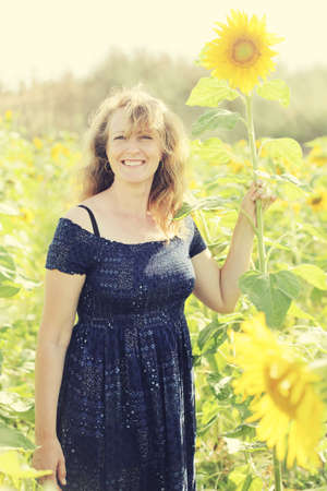 Beauty mature woman with sunflower enjoying freedom on summer sunflower fieldの写真素材