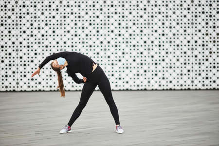 A young girl trains on the street in a black tracksuit. The white textured wall of the city building in the background. Empty space for your text.の写真素材
