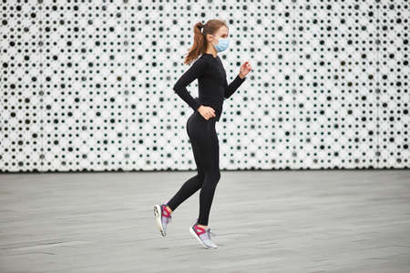 A young girl trains on the street in a black tracksuit. The white textured wall of the city building in the background. Empty space for your text.の写真素材