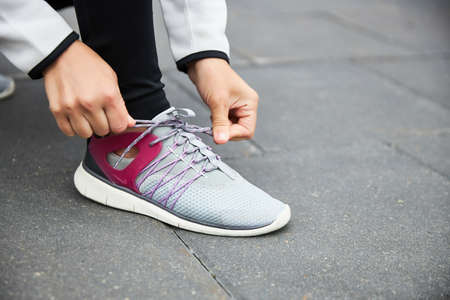 Sports sneaker close-up on the asphalt. The girl ties her shoelaces before jogging.の写真素材