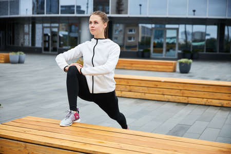 A young girl in a tracksuit warms up before jogging in the urban environment.の写真素材