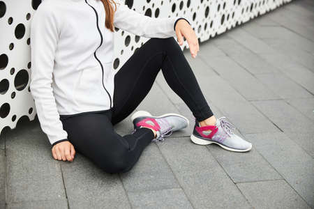 A girl in a white tracksuit rests after a sport near the city wall.の写真素材