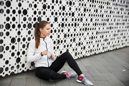 A girl rests and drinks water after sports in the city.の写真素材