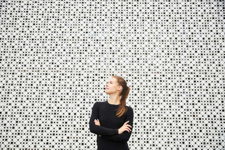 A girl in a black tracksuit stands against the white city texstud wall. A place for text.の写真素材